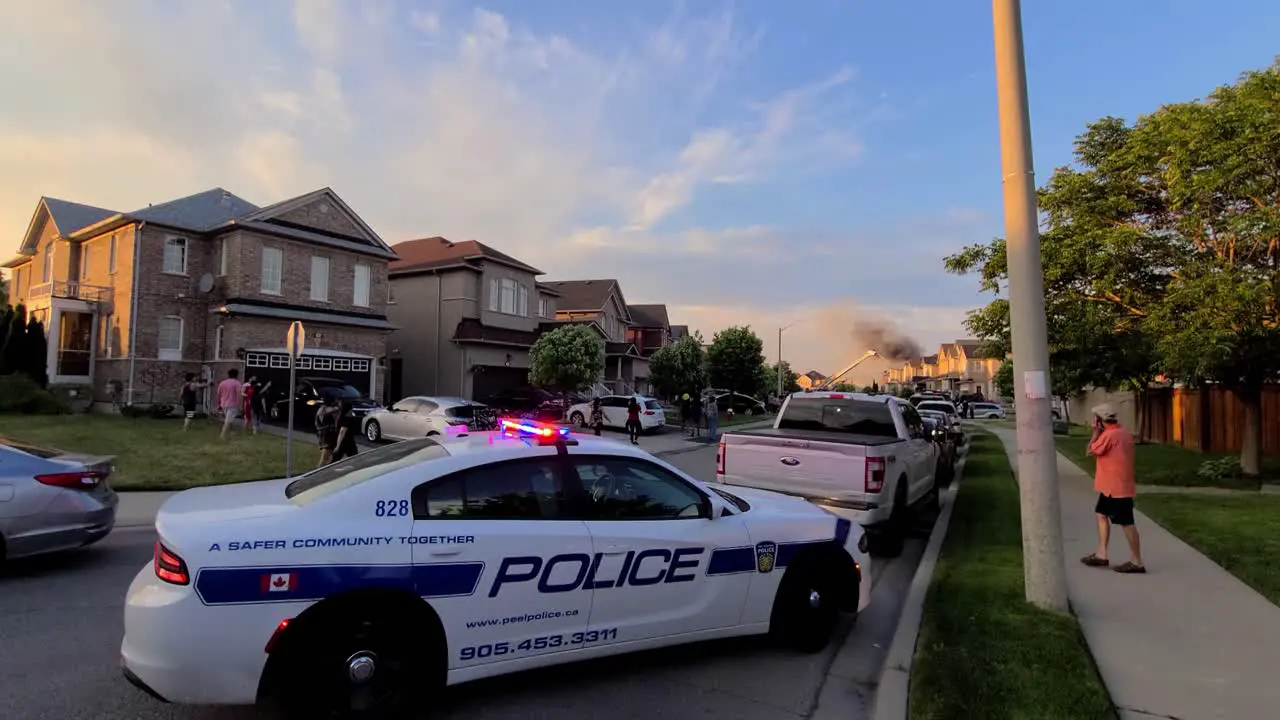 Scene of a neighborhood house fire with a police car in the foreground