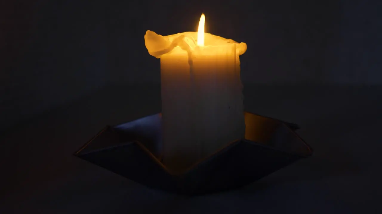 Slow moving shot around a lit candle in a dark room in full frame