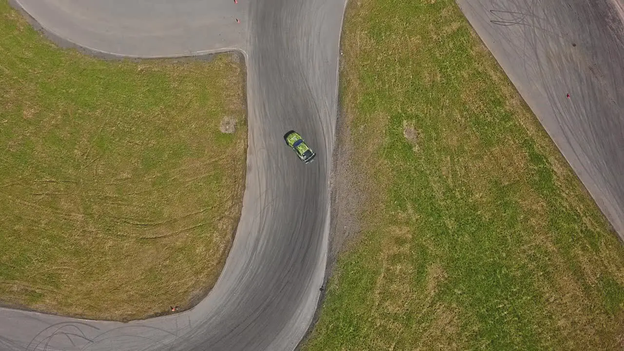 Aerial shot of a car drifring on high speed on a turn green grass and a race track top view shot