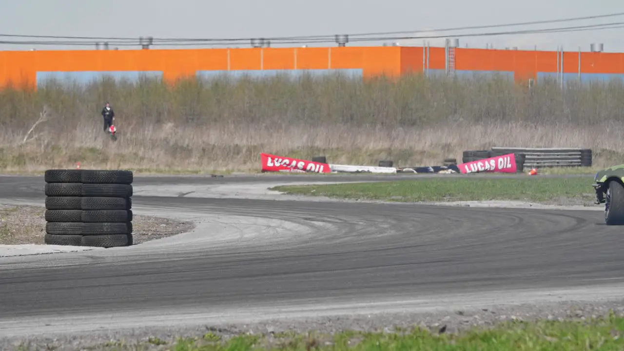 Slow motion shot of a drifting green car on a race track with a pile of tires and s turn