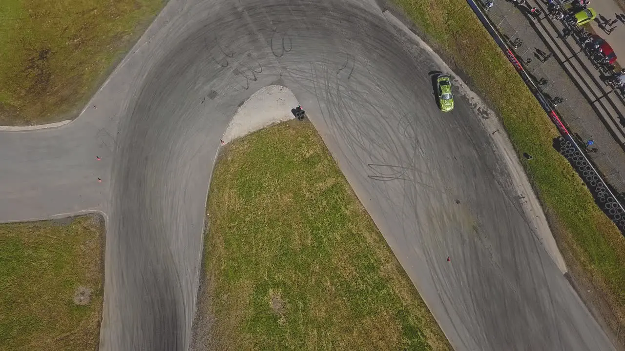 Aerial shot of a car drifring on high speed on a turn green grass and a race track top view shot next to viewers