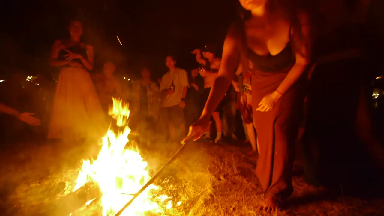 Asian woman managing ceremonial fire with stick at dance performance during night filmed handheld as wide shot