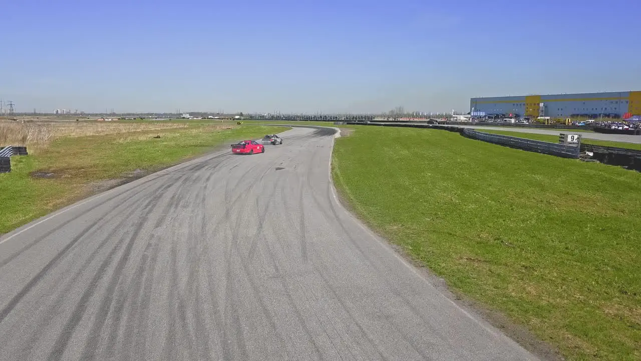 Aerial drift cars passing by on a race track red and brown car with tire skids and green grass