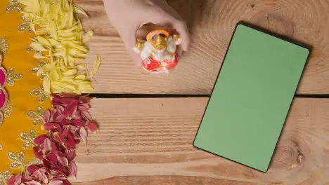 Hand Picking Up Statue Of Ganesh On Table With Green Screen Digital Tablet In Festival Of Diwali