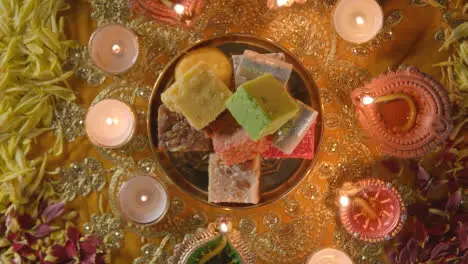 Overhead Shot Of Hands Picking Up Indian Sweets In Bowl On Table Decorated To Celebrate Festival Of Diwali