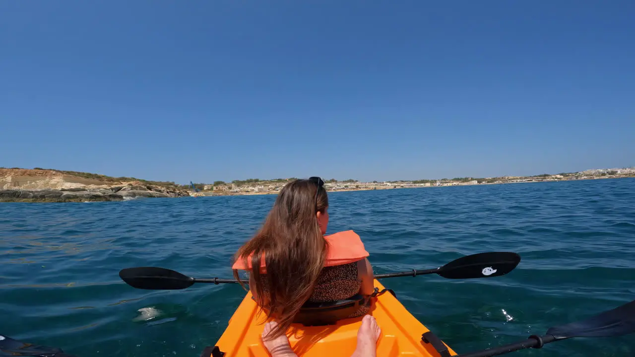 Woman wearing sunglasses on her head sways in a kayak on the clear blue waters of Malta