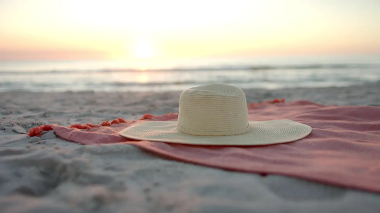 A diverse sun hat rests on a beach towel at sunset with copy space