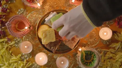 Overhead Shot Of Hand Picking Up Indian Sweets In Bowl On Table Decorated To Celebrate Festival Of Diwali 1