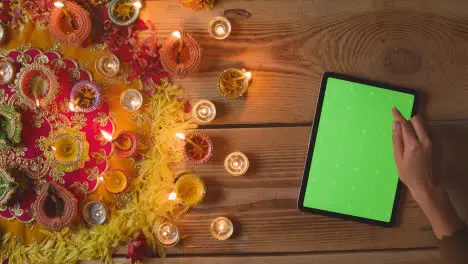 Overhead Shot Of Person Using Green Screen Digital Tablet With Burning Lamps Celebrating Festival Of Diwali