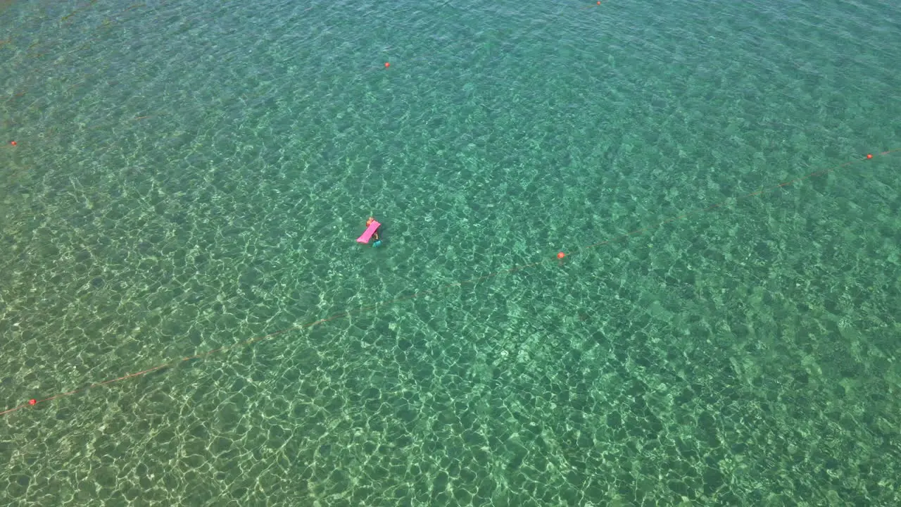 Tourist With Airbed Swimming In The Middle Of The Tropical Crystal Clear Sea During Summer In Sardinia Italy aerial top down