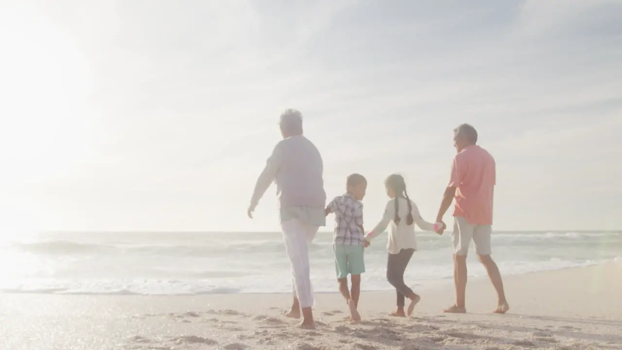 Happy hispanic grandparents and grandchildren walking on beach at sunset