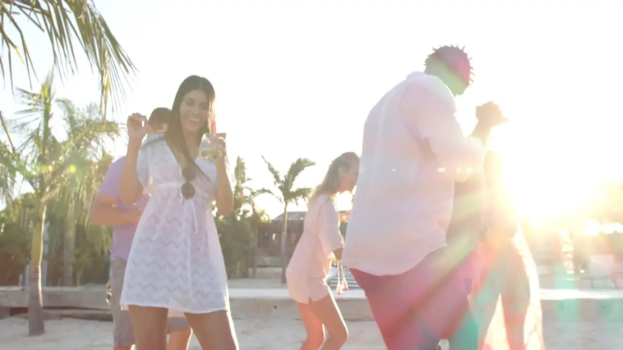 Happy diverse group of friends dancing holding cocktails at beach