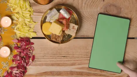 Overhead Shot Of Indian Sweets In Bowl On Table Decorated To Celebrate Festival Of Diwali With Digital Tablet