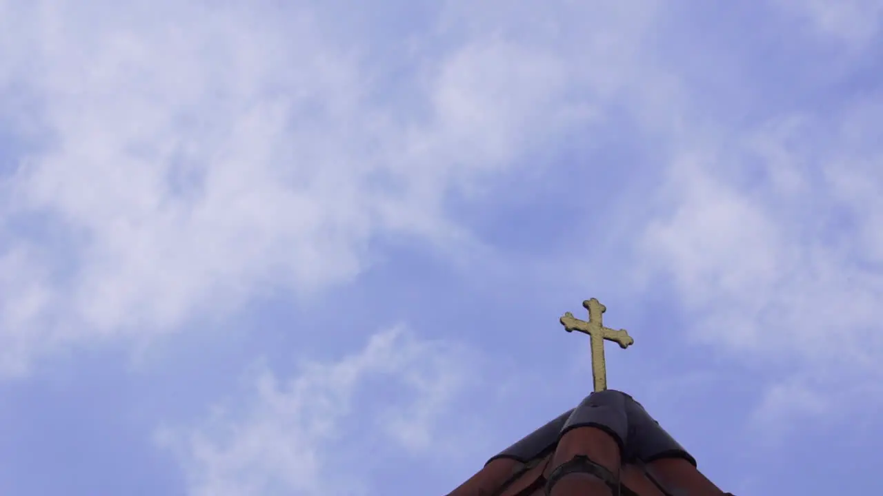 Catholic church roof golden cross with fast clouds and blue sky