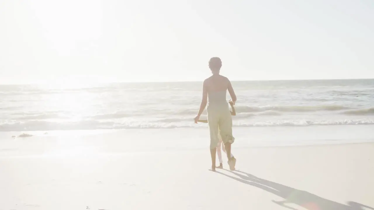 Happy african american mother and daughter walking at beach in slow motion