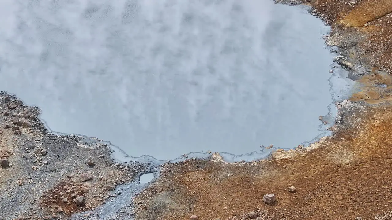 An aerial drone's fixed view of the muddy border with steam at Engjahver's steam lake on the Reykjanes Peninsula in Iceland