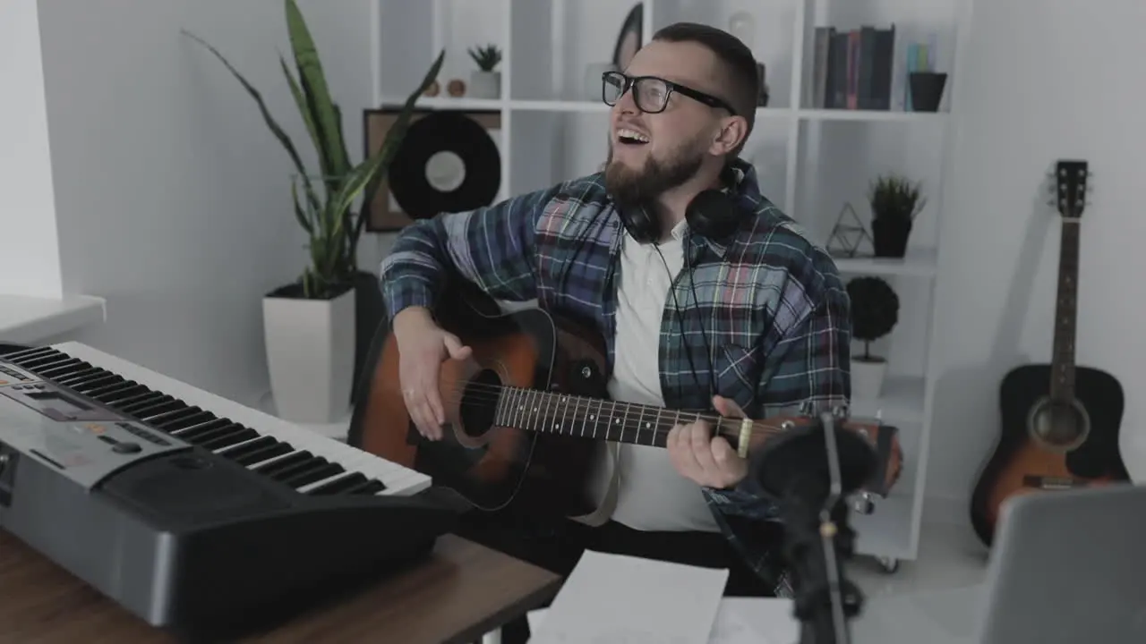 Male Musician Singing And Playing Guitar Next To His Electric Keyboard At Home