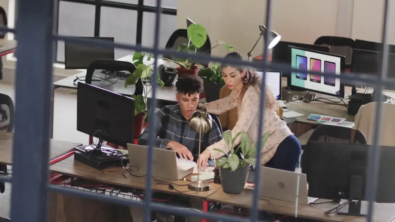 Two diverse creative designers in discussion at computer in casual office slow motion