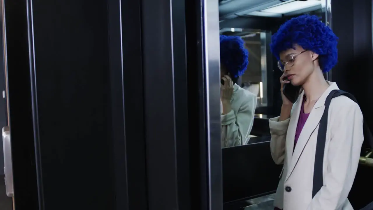 Biracial businesswoman with blue afro talking on smartphone and using elevator slow motion