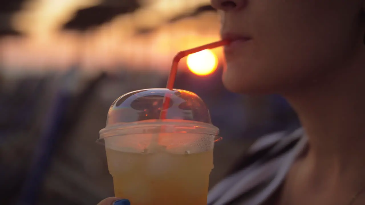 Woman having iced drink on the beach at sunset