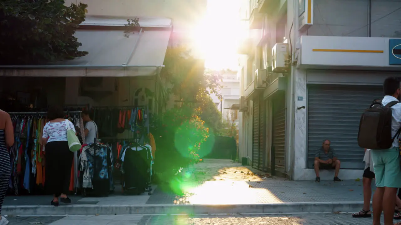 Street with people and vendor selling clothes View in bright sunshine Greece