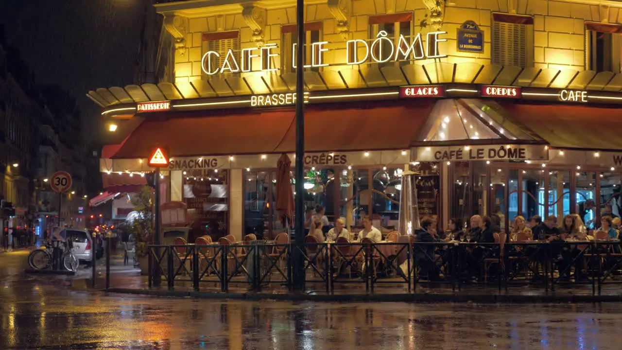 Parisian street with people in cafe view at rainy night