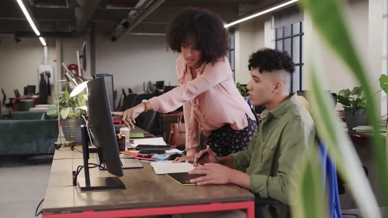 Two happy diverse creative designers in discussion at computer in casual office slow motion