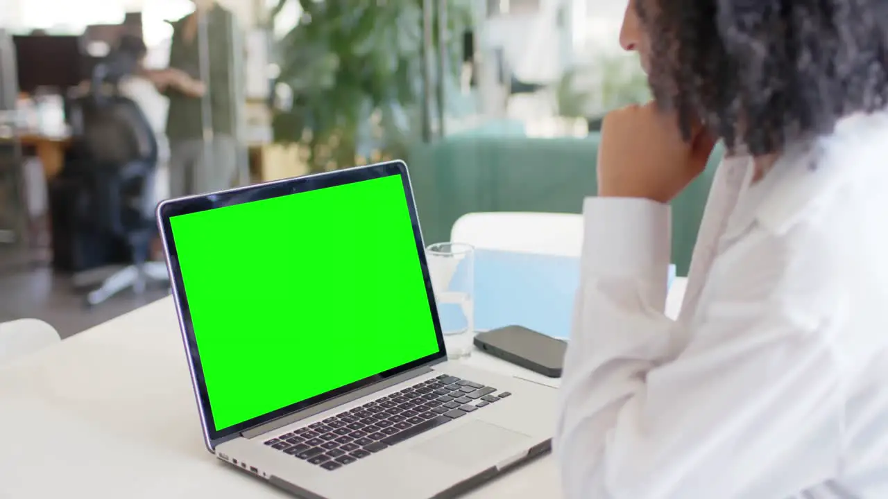 Biracial businesswoman watching laptop with green screen in office slow motion