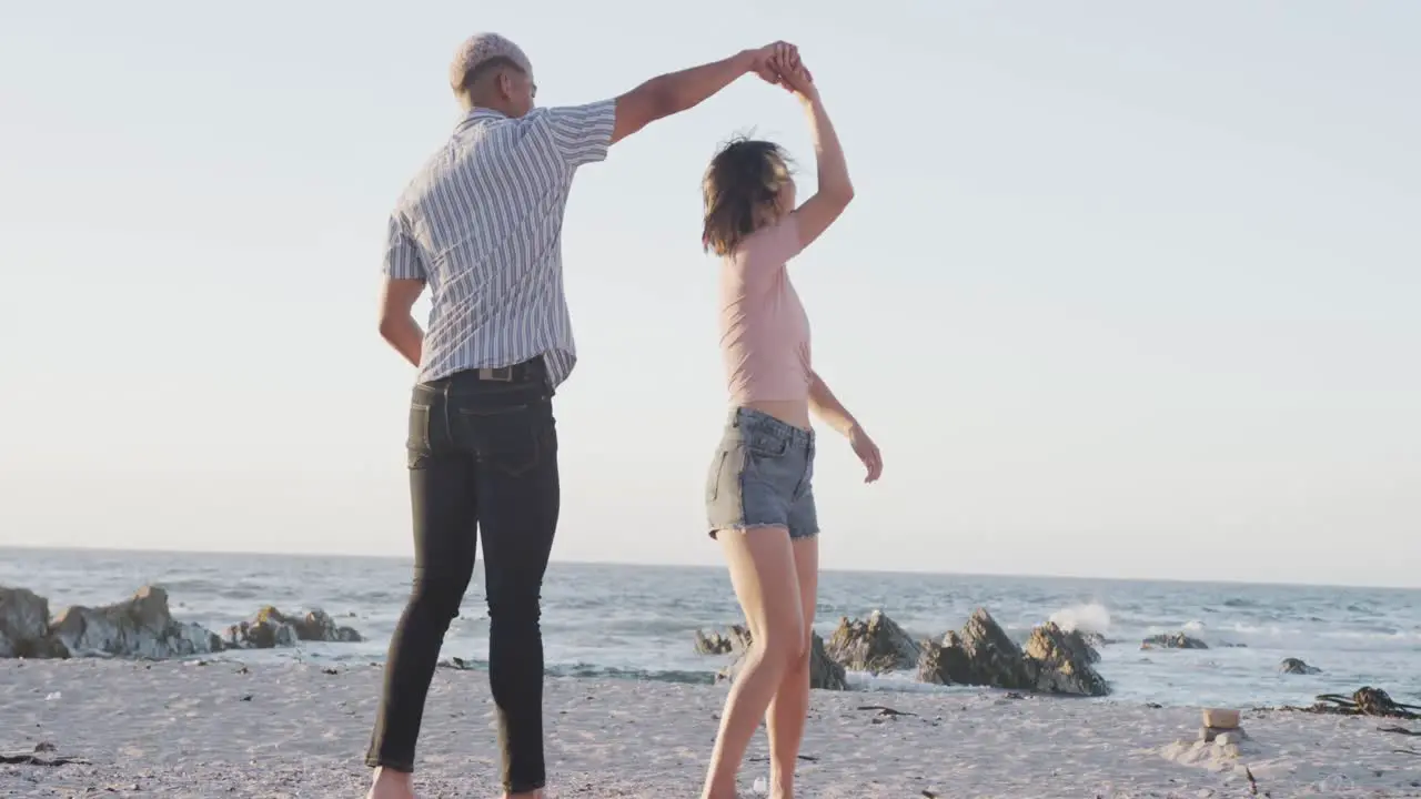 Happy biracial couple dancing together at beach in slow motion