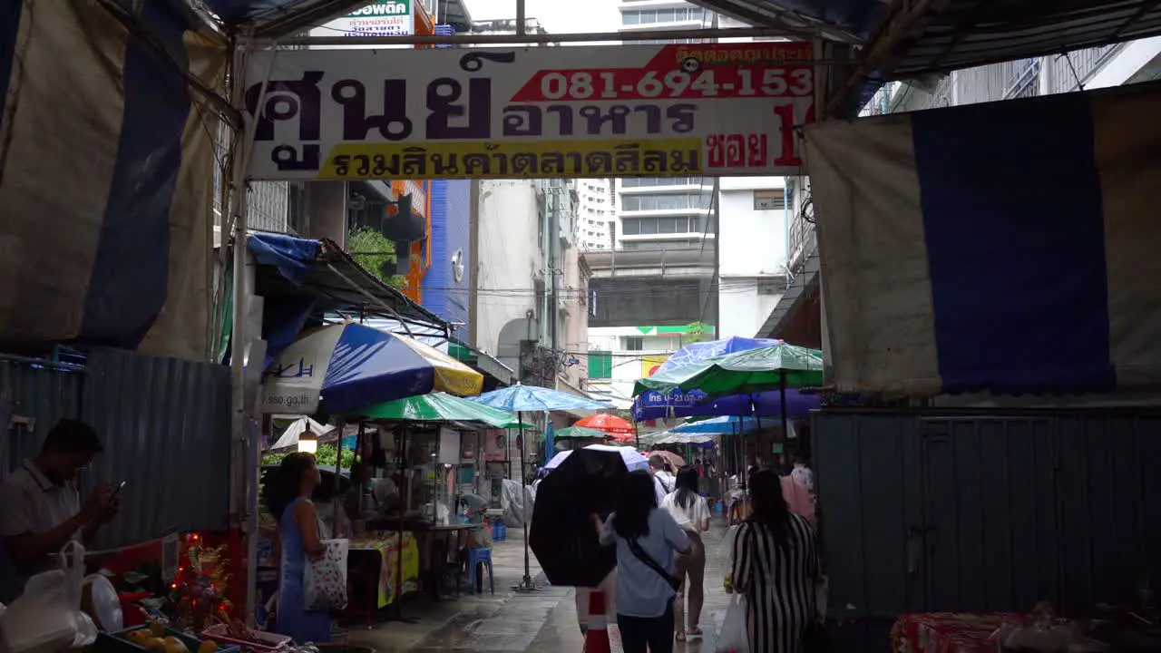 View of people using umbrellas on rainy days exiting the entrance of the local market in Silom Soi 10 Bangkok Thailand