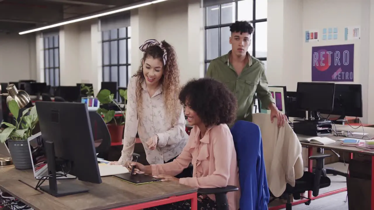 Two happy diverse female creative designers in discussion at computer in casual office slow motion