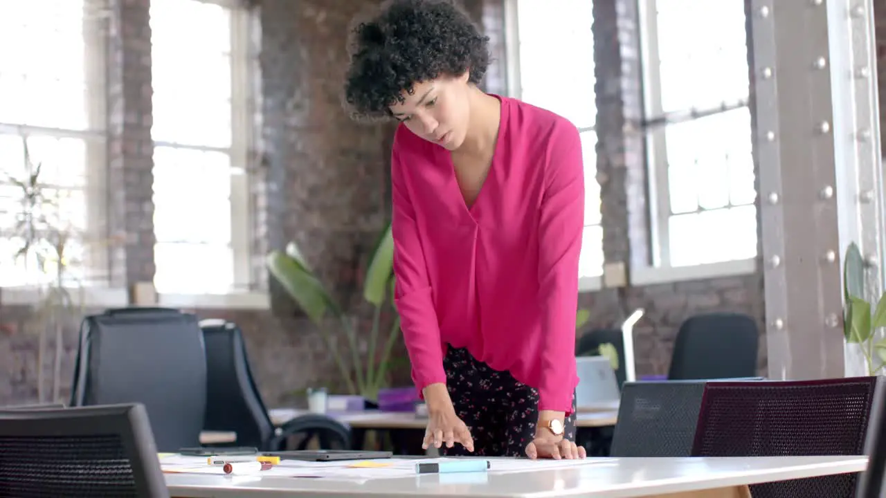 Focused biracial casual businesswoman checking documents on table in office in slow motion