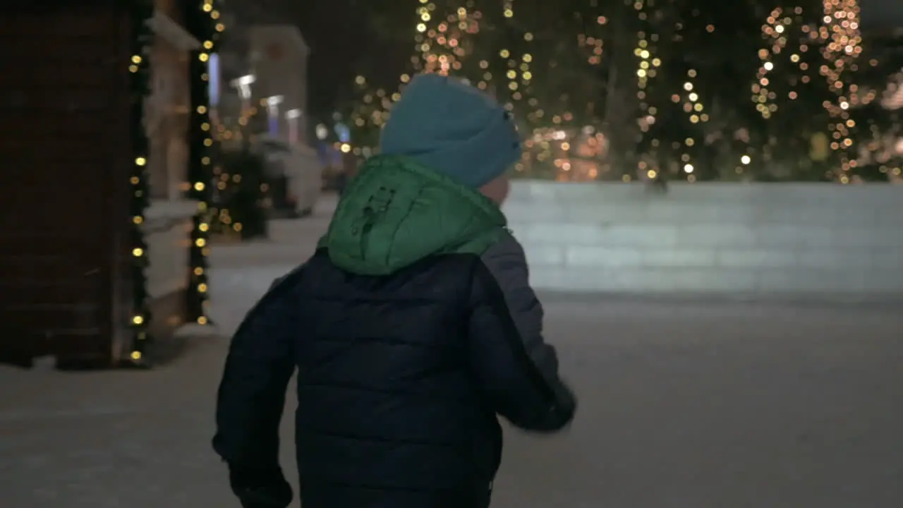 Child running in snowy street with Christmas lights