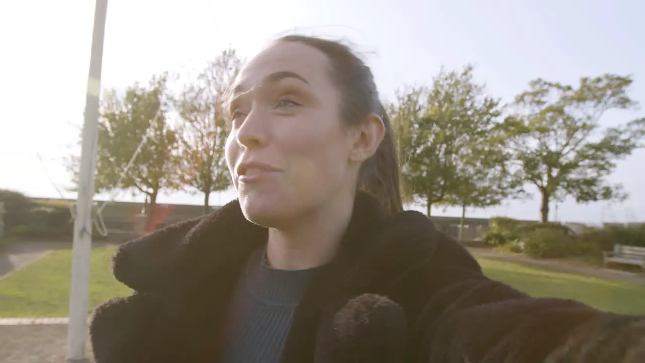 Female smiling and talking to camera on a videocall in a park with beautiful lens flare