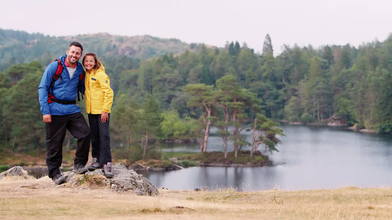 Caucasian father and daughter on the left of shot standing on rock by a lake in the countryside looking to camera Lake District UK