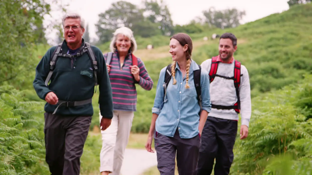 Two mixed age couples walking on a countryside path during family camping adventure Lake District UK