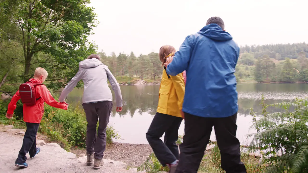 Young family walking to a lake and playing at the shore back view Lake District UK