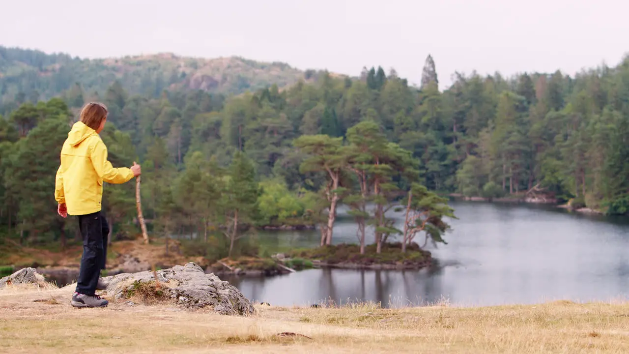 A girl walks into the left of shot to stand on a rock and admire the lakeside view back view Lake District UK