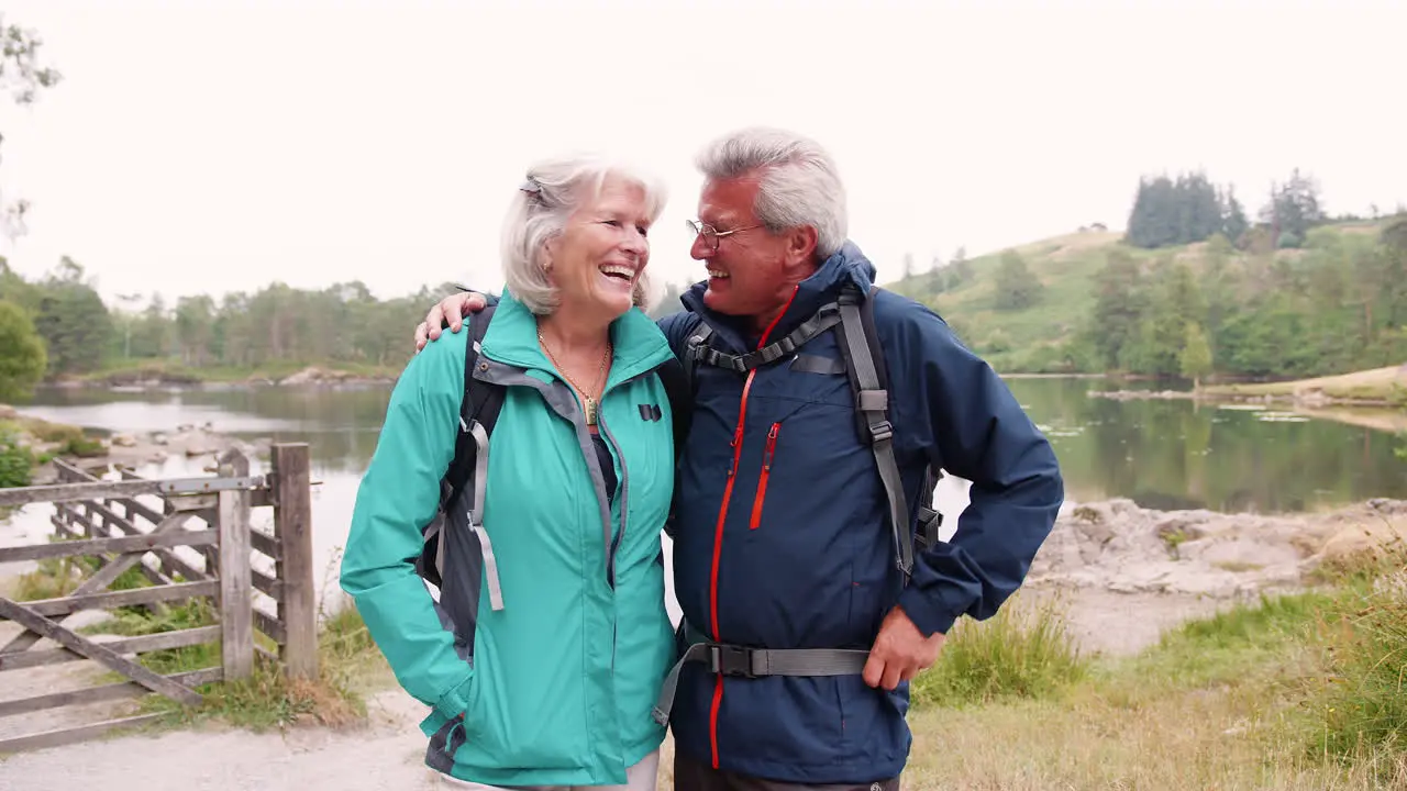 Senior couple on a camping holiday standing by a lake laughing close up Lake District UK