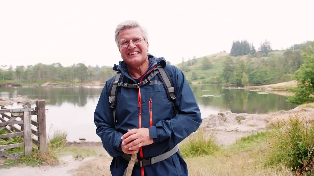 Happy middle aged Caucasian man standing near the shore of a lake holding a stick close up Lake District UK