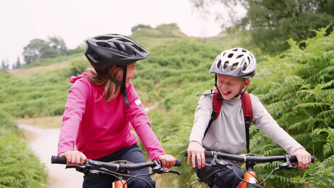 Two children sitting on their mountain bikes on a country path laughing Lake District UK