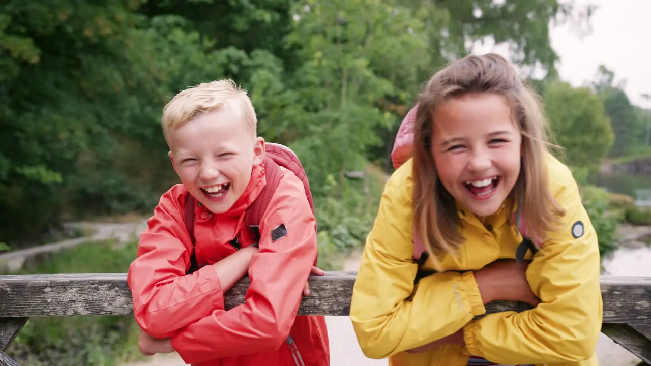 Brother and sister leaning on a wooden fence in the countryside laughing close up Lake District UK