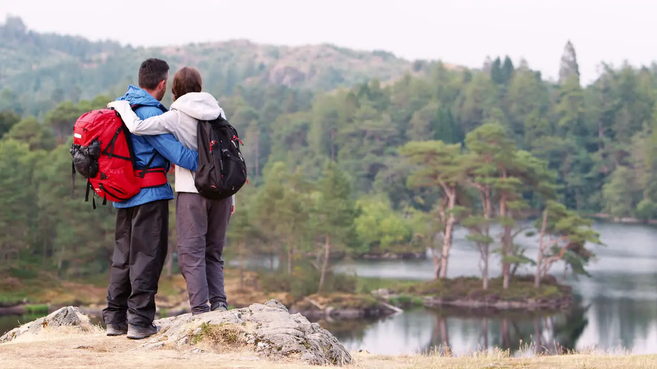 Young adult couple on the left of shot standing in the countryside admiring a lake view back view Lake District UK