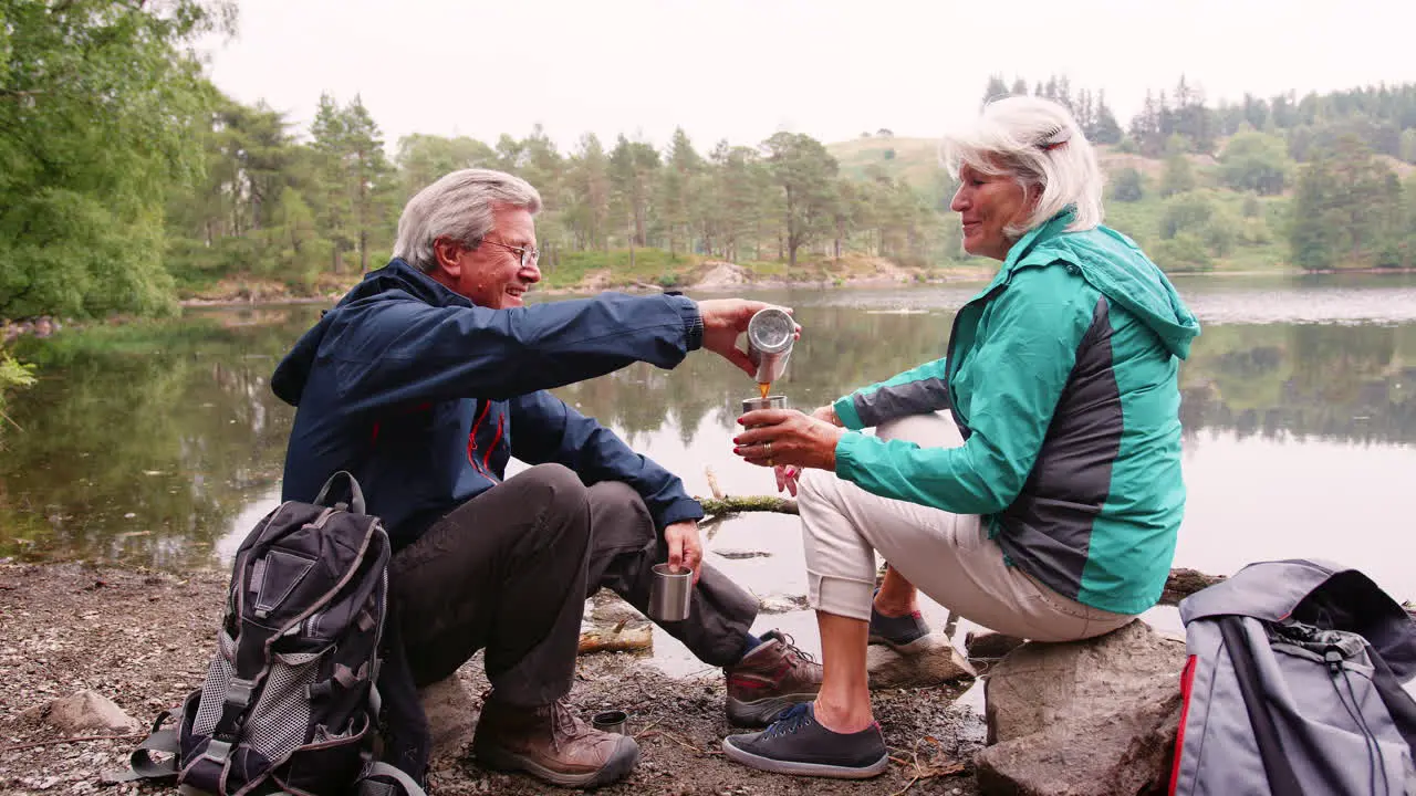 Senior couple sitting by a lake drinking coffee during camping holiday Lake District UK