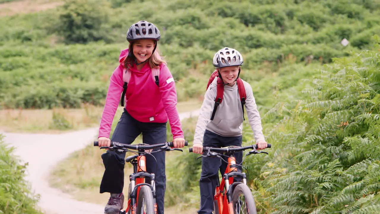 Two children having fun on mountain bikes in the countryside ride past the camera and out of shot Lake District UK