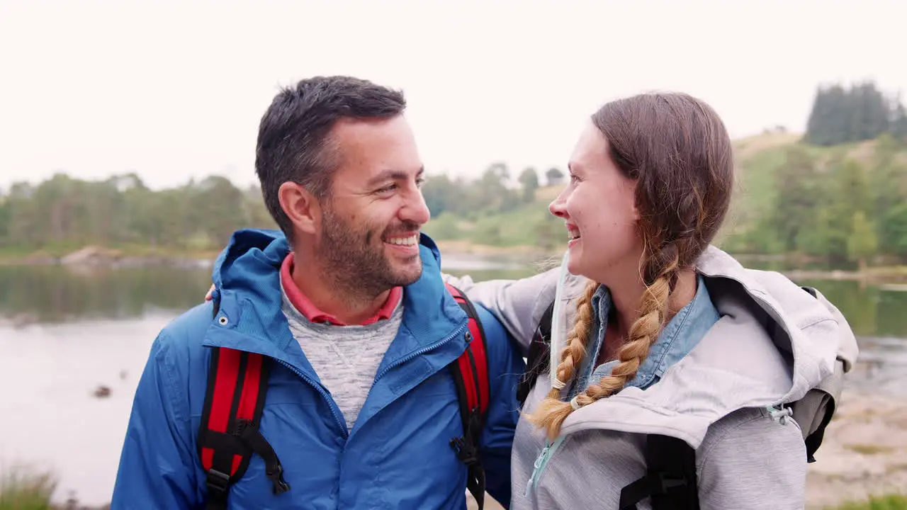 Young adult couple standing on a camping trip standing near a lake looking at camera close up Lake District UK