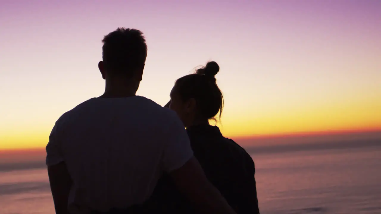 Couple standing on a beach by the sea at sunset