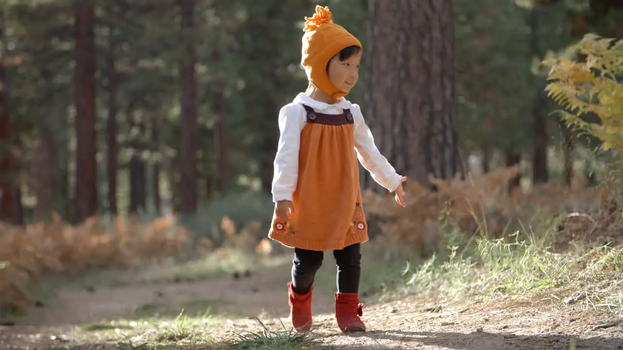 Asian toddler girl walking alone in a forest front view