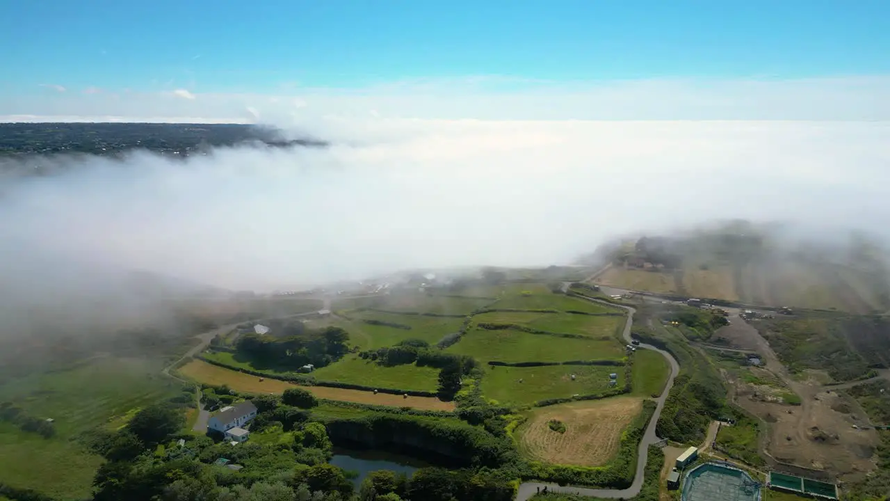 The fog coming in off the sea over fields in Guernsey on otherwise bright sunny day aerial footage