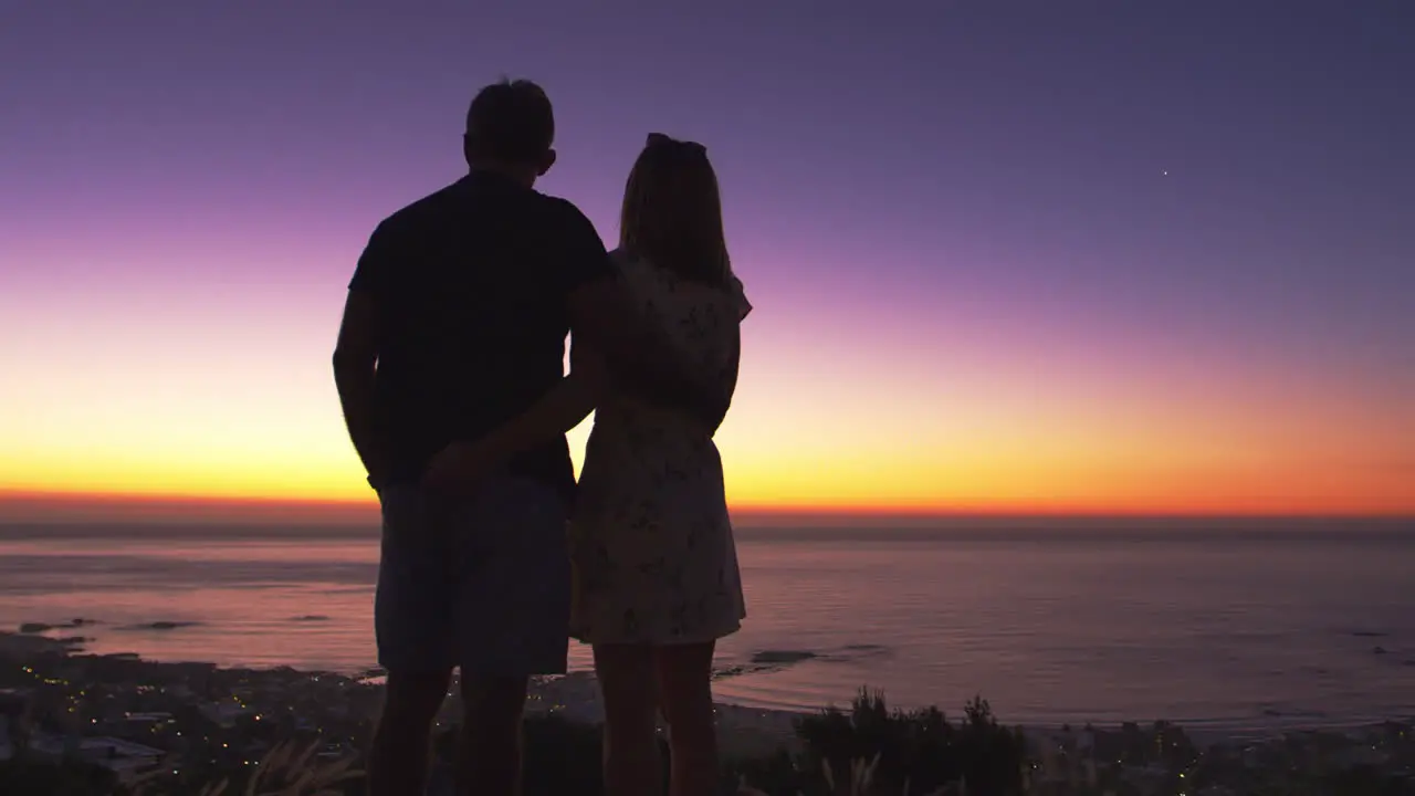 Couple standing on a beach by the sea at sunset silhouette